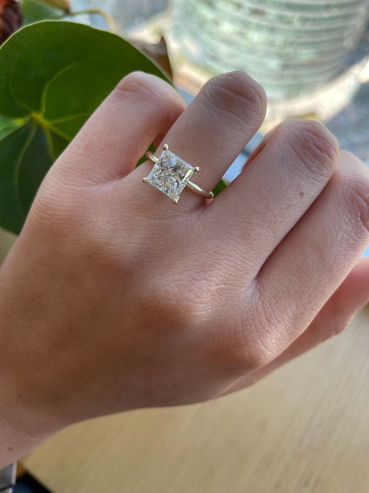 a woman's hand with a diamond ring on top of her finger and a plant in the background