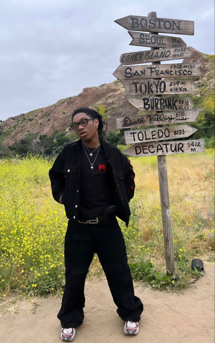 a man standing in front of a sign pointing to different destinations on the side of a road