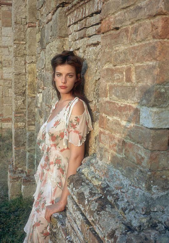 a woman leaning against a stone wall with her hands in her pockets