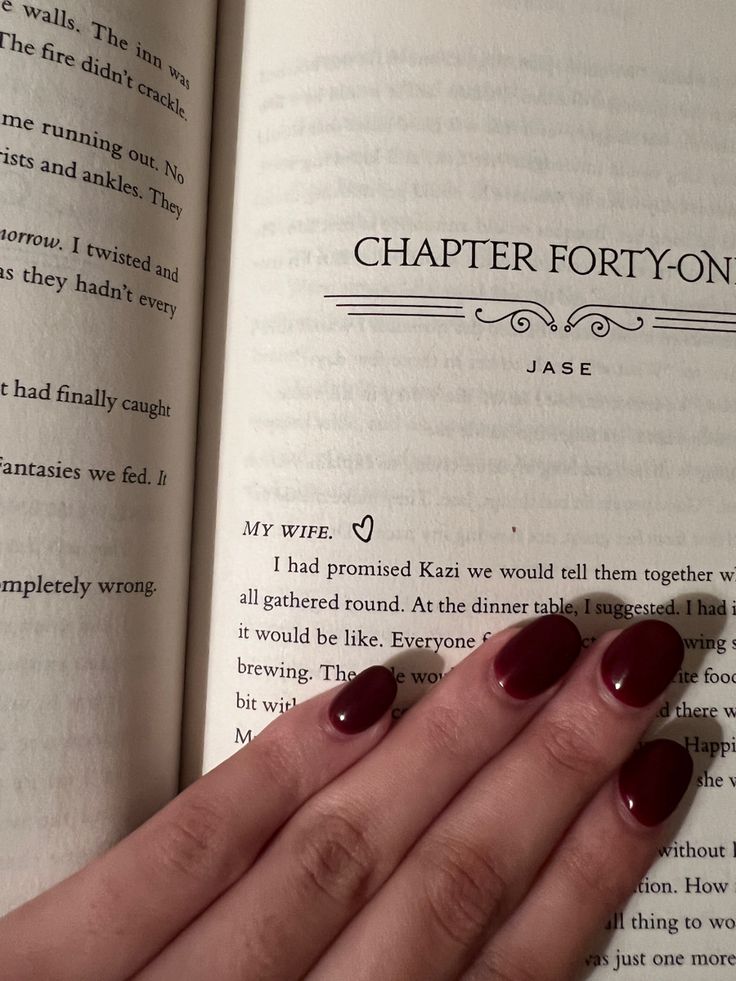 a woman's hand with red nail polish on her nails holding an open book