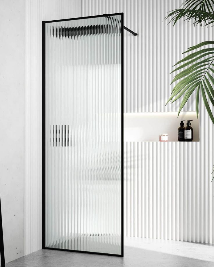 a white and black bathroom with a plant in the corner next to the shower door