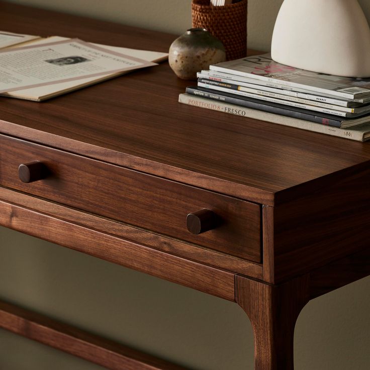 a wooden table topped with books next to a white vase and other items on top of it