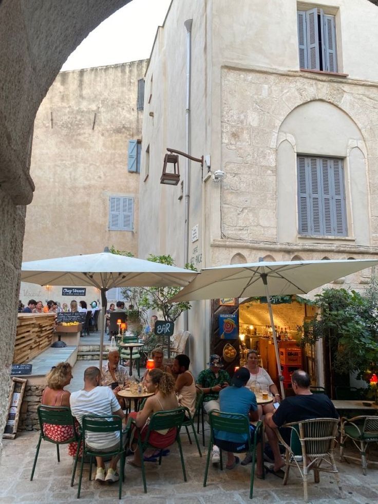 people are sitting at tables under umbrellas in front of an old building on the street