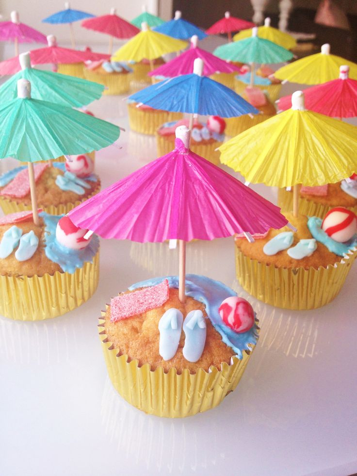 cupcakes decorated with umbrellas and beach balls are on a white tablecloth