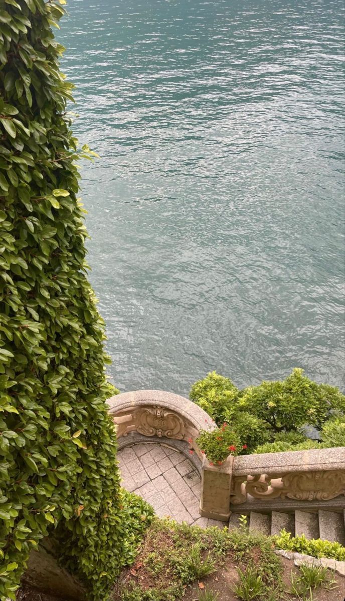 a bench sitting on top of a lush green hillside next to the ocean with an umbrella over it