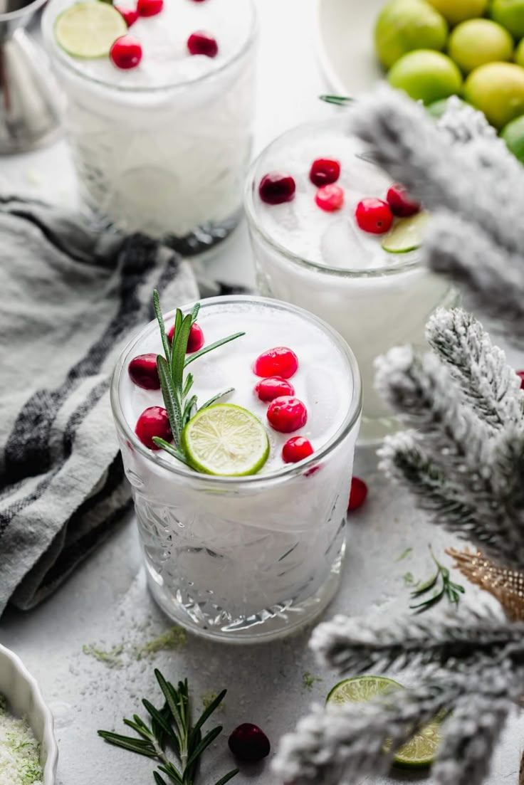 two glasses filled with white wine and garnished with cranberries, limes and rosemary