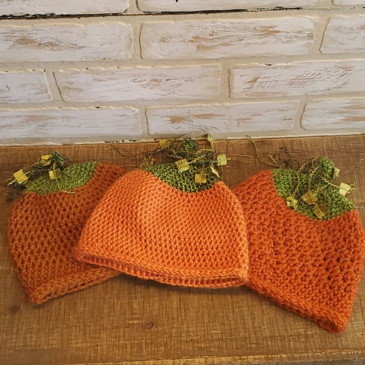 three knitted pumpkin hats sitting on top of a wooden table