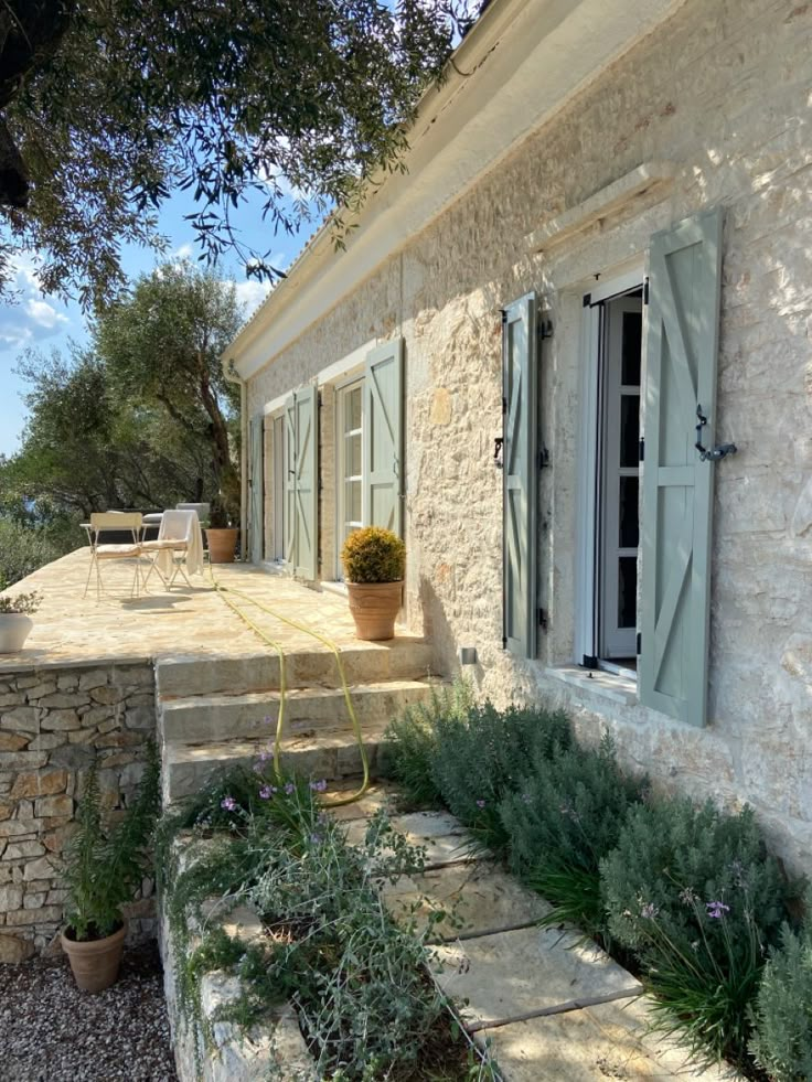 a stone house with green shutters and plants