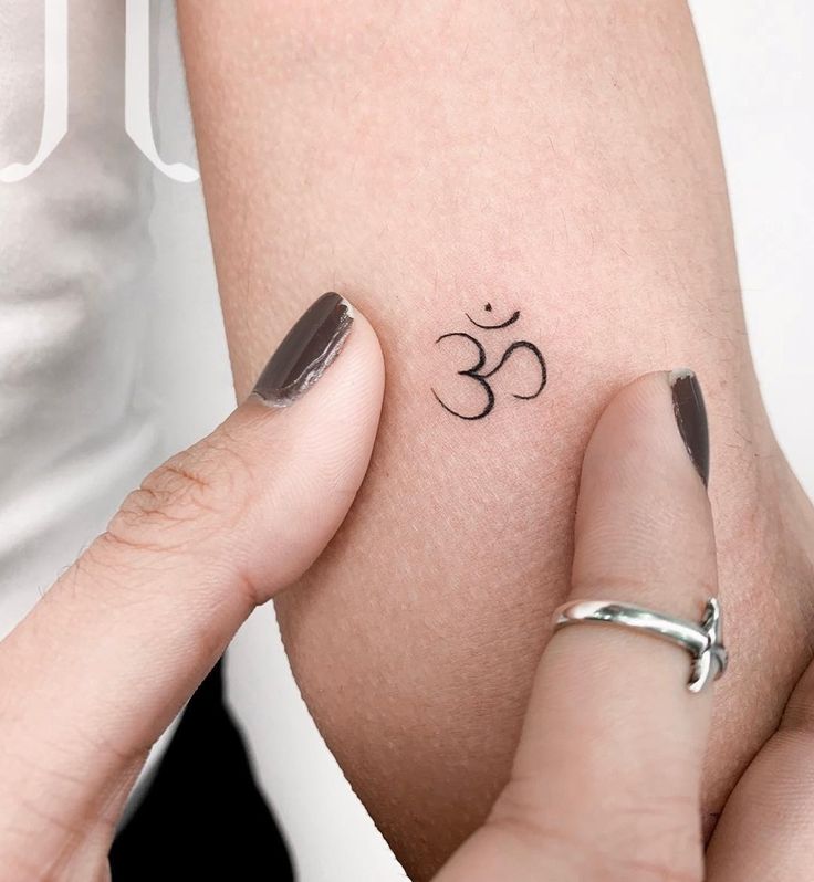 two hands holding each other with small tattoos on their arm and wrist, both showing the symbol