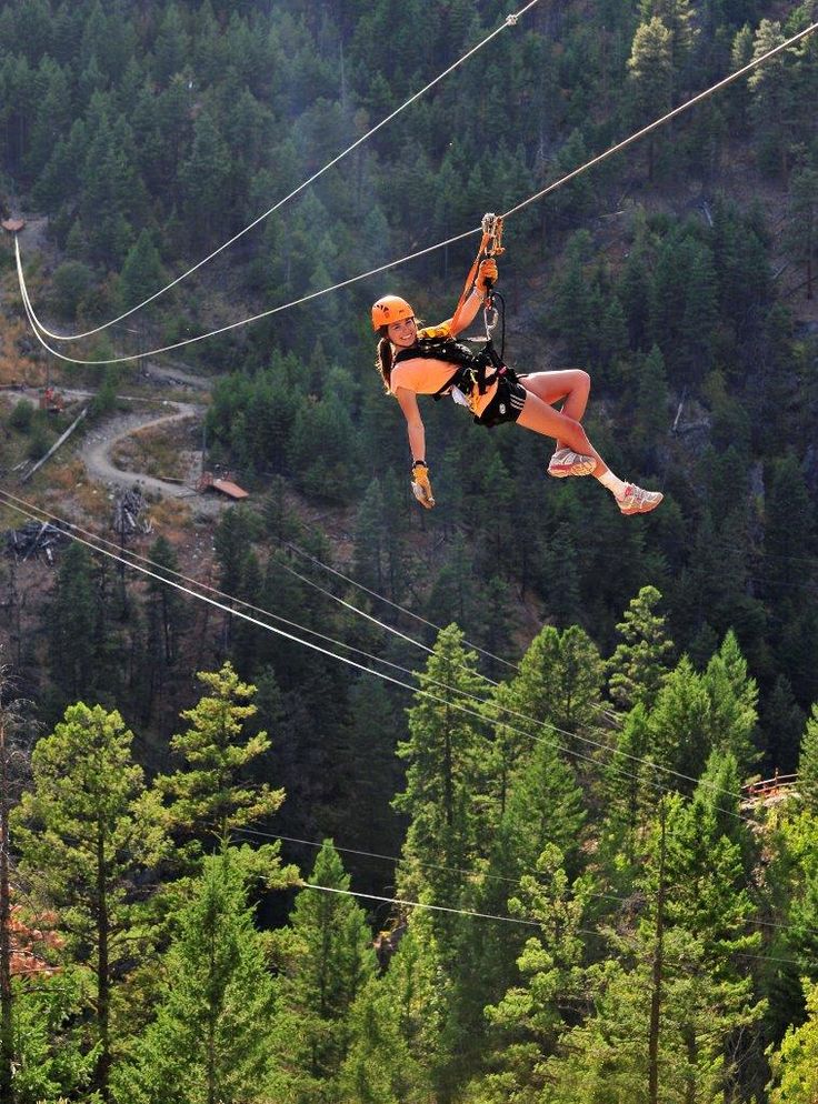 a woman is zipping through the air on a rope line in front of some trees