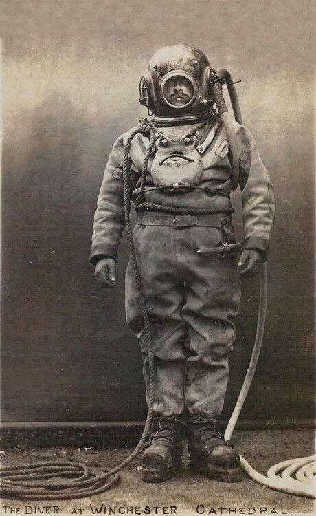 an old black and white photo of a man in a diving suit holding a hose