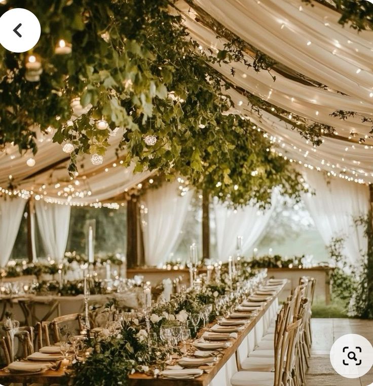 an outdoor tent with tables and chairs covered in greenery