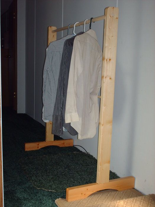 clothes are hanging on wooden racks in the corner of a room with green carpeted flooring