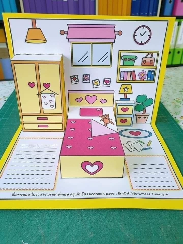 an open card with a doll house in it on a table next to bookshelves