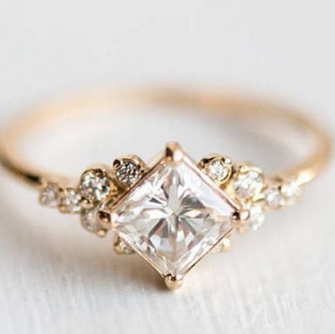 a gold ring with a princess cut diamond surrounded by small white and clear stones on the band