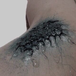 the back of a woman's shoulder with water on it and drops of blue paint