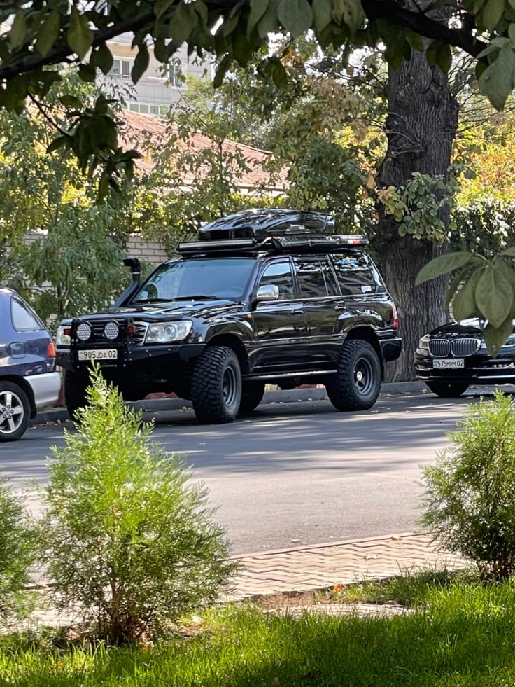 two suvs are parked on the side of the road in front of some trees