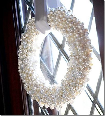 a wreath with pearls hanging from the side of a glass door next to a window