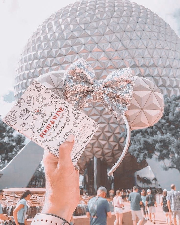 a hand holding up a disney mouse ears with the top of it's head in front of a building