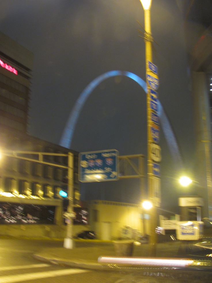 the arch is lit up at night in front of an office building and street sign