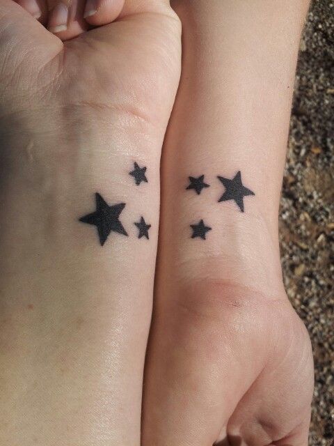 two people holding hands with small black stars tattooed on their wrists, both showing the same tattoo design