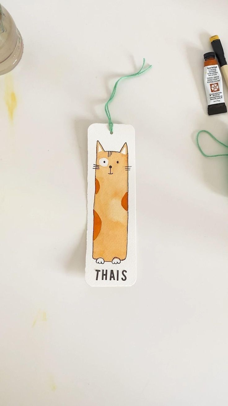 an orange cat is hanging from a string next to some crafting supplies on a table