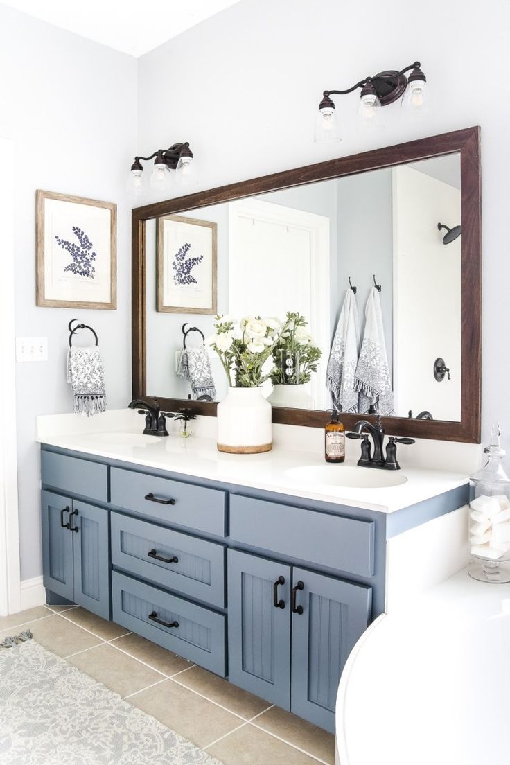 a bathroom with blue cabinets and white counter tops is pictured in this image, there are two mirrors on the wall above the sink