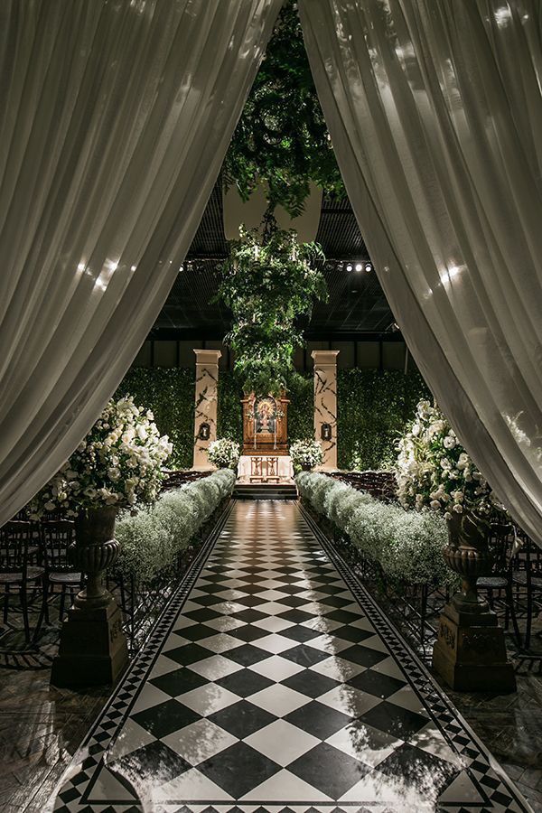 an indoor wedding venue with white drapes and greenery on the ceiling, black and white checkered floor