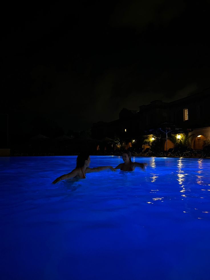 two people swimming in a pool at night