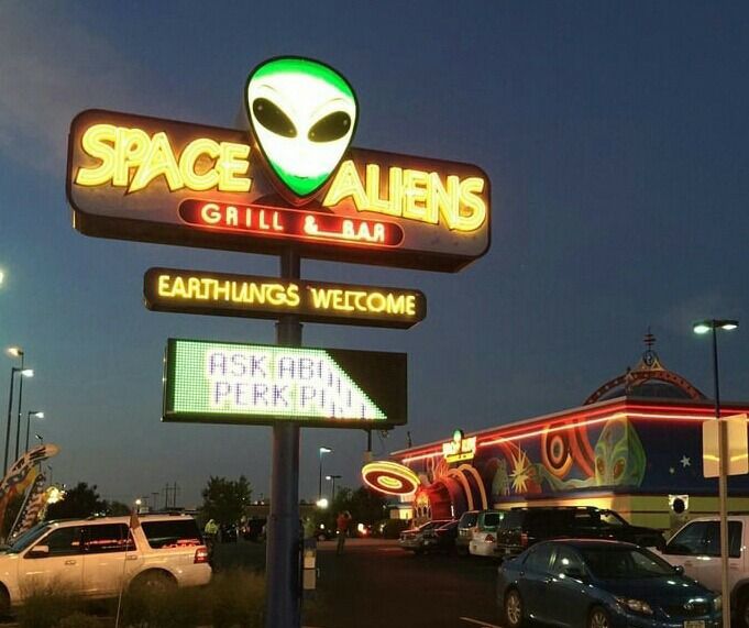 the sign for space aliens grill and bar is lit up at night with cars parked in front