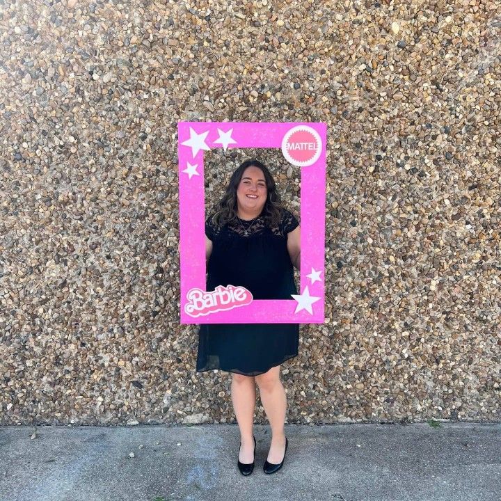 a woman standing in front of a wall holding a barbie photo frame