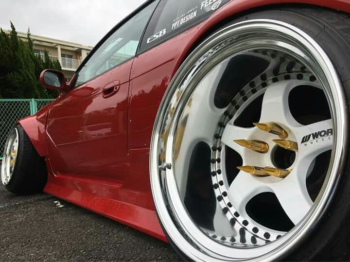 a red sports car with gold rims parked in a parking lot next to a fence