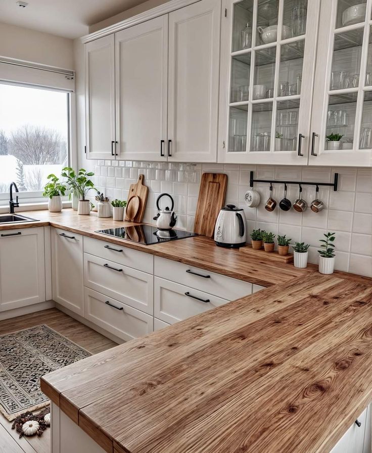 a kitchen with white cabinets and wooden counter tops in front of a large window that has potted plants on it