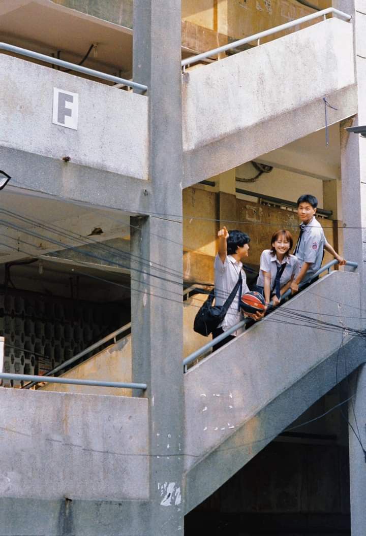 three children are riding down the escalator in an apartment building while one boy is on his cell phone