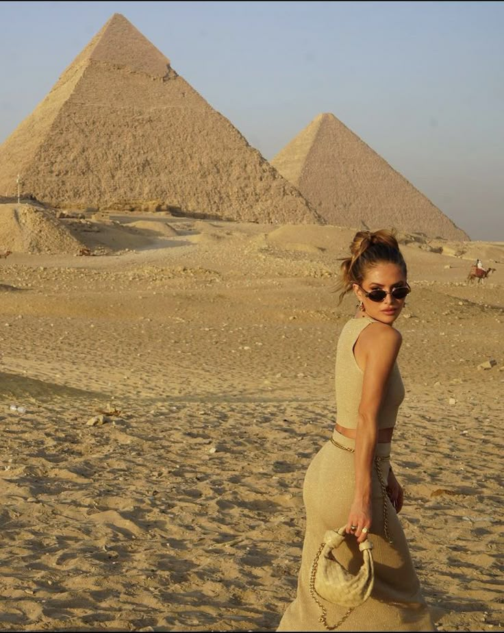 a woman walking on the sand in front of three pyramids