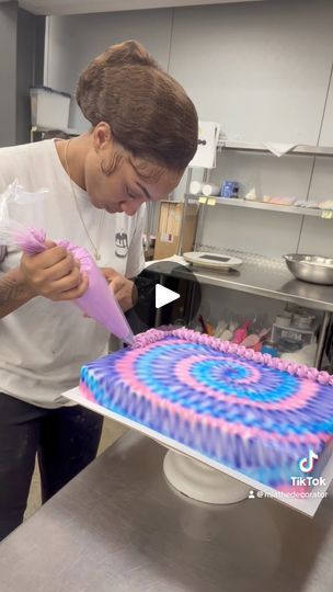 a woman is decorating a cake with pink and blue icing