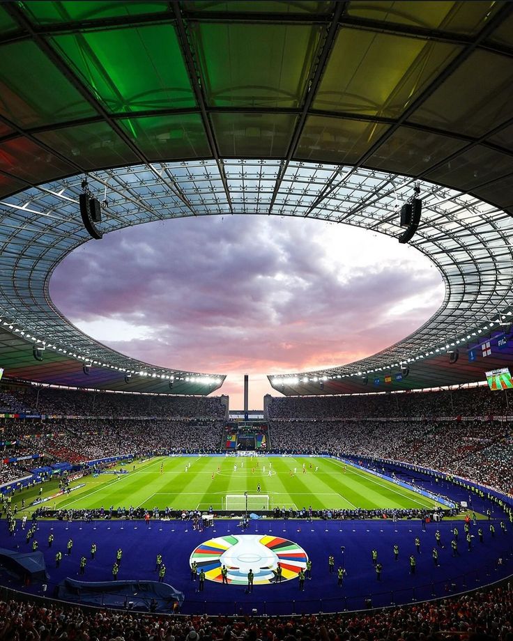 a stadium filled with lots of people watching a soccer game at sunset or sunrise time