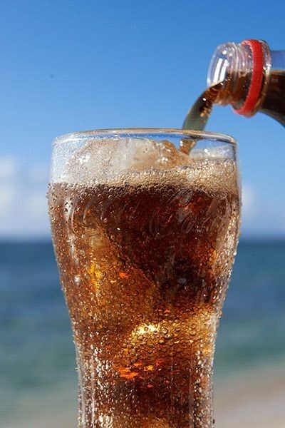 a glass filled with liquid sitting on top of a beach