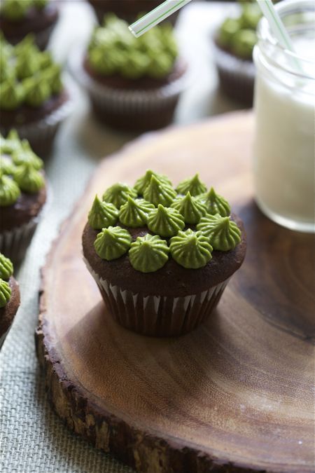 chocolate cupcakes with green frosting and sprinkles on a wooden tray