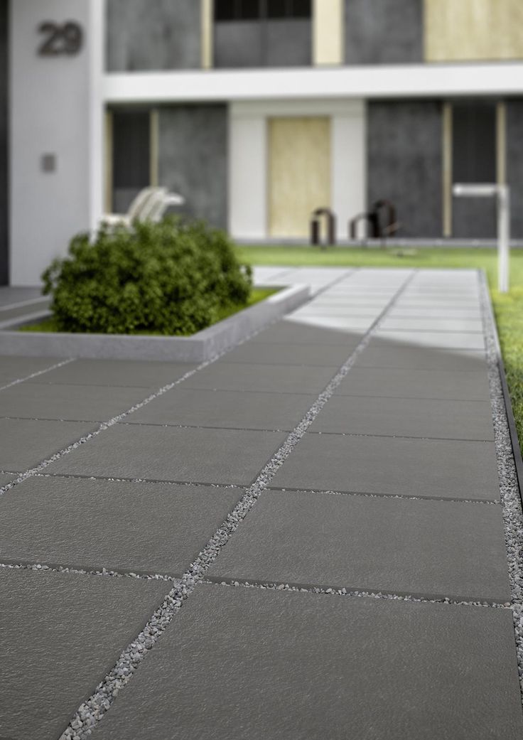 a concrete walkway in front of a building with grass and bushes on the side walk