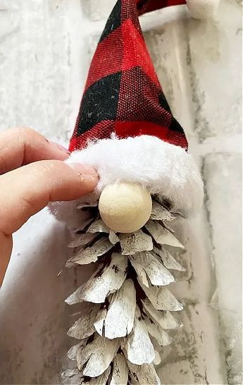 a hand holding a pine cone with a santa hat on it