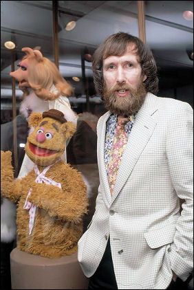 a man in a suit and tie standing next to two stuffed animals, one with a beard