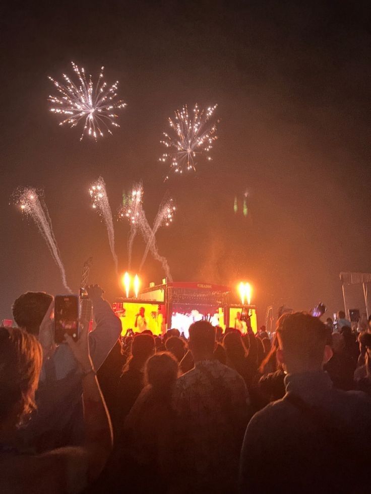 fireworks are lit up in the night sky at an outdoor music festival with people watching