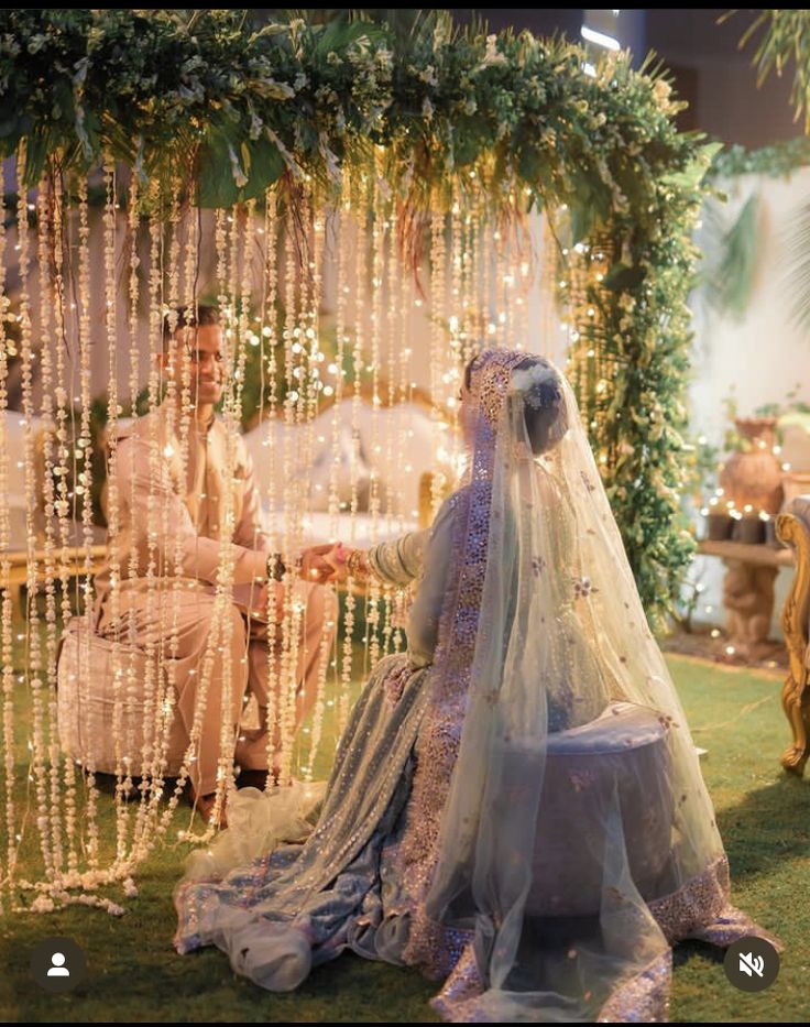 a bride and groom sitting in front of a decorated stage with lights on the walls