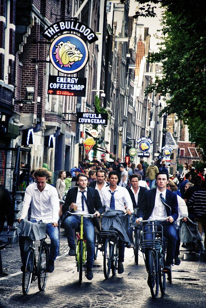 a group of men riding bikes down a street next to tall buildings with signs above them