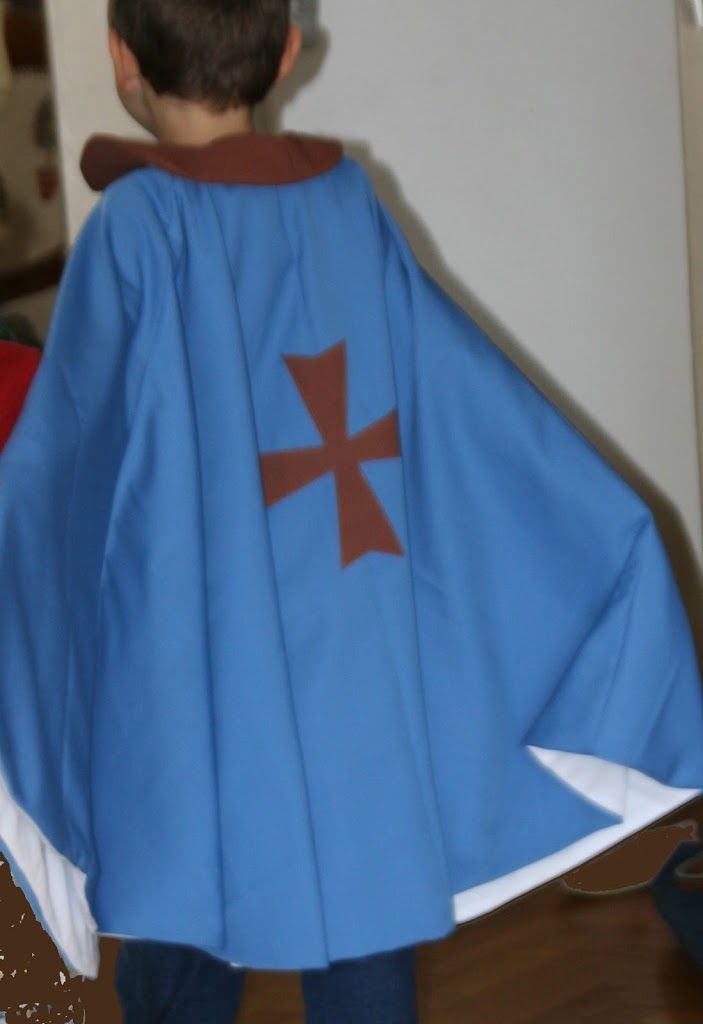 a young boy dressed in a blue cape and brown cross on it's chest