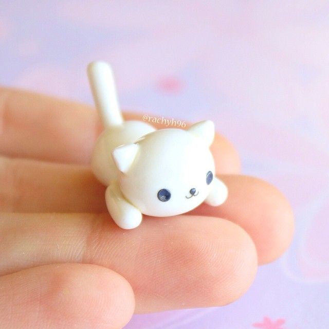 a tiny white cat sitting on top of a person's finger in front of a pink background