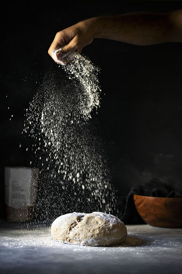 a person sprinkling flour on top of a doughnut