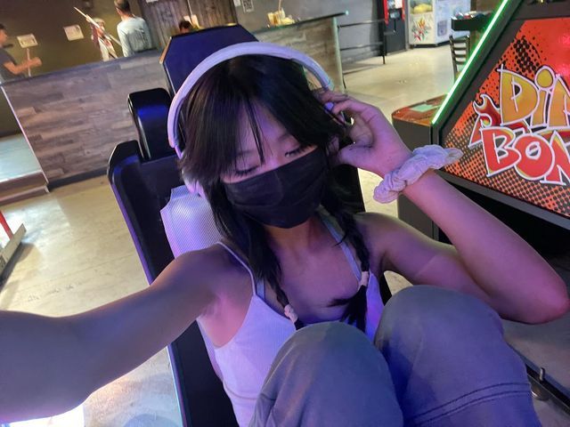 a woman wearing a mask and sitting in front of a video game machine with her hands on her face