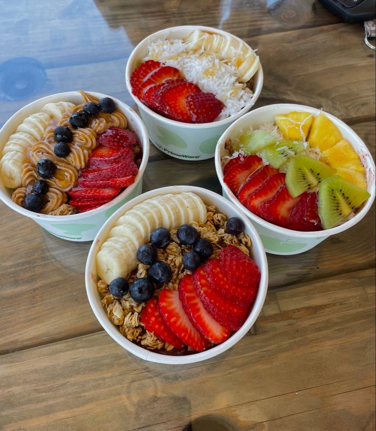 four bowls filled with different types of food on top of a wooden table next to a cup of coffee